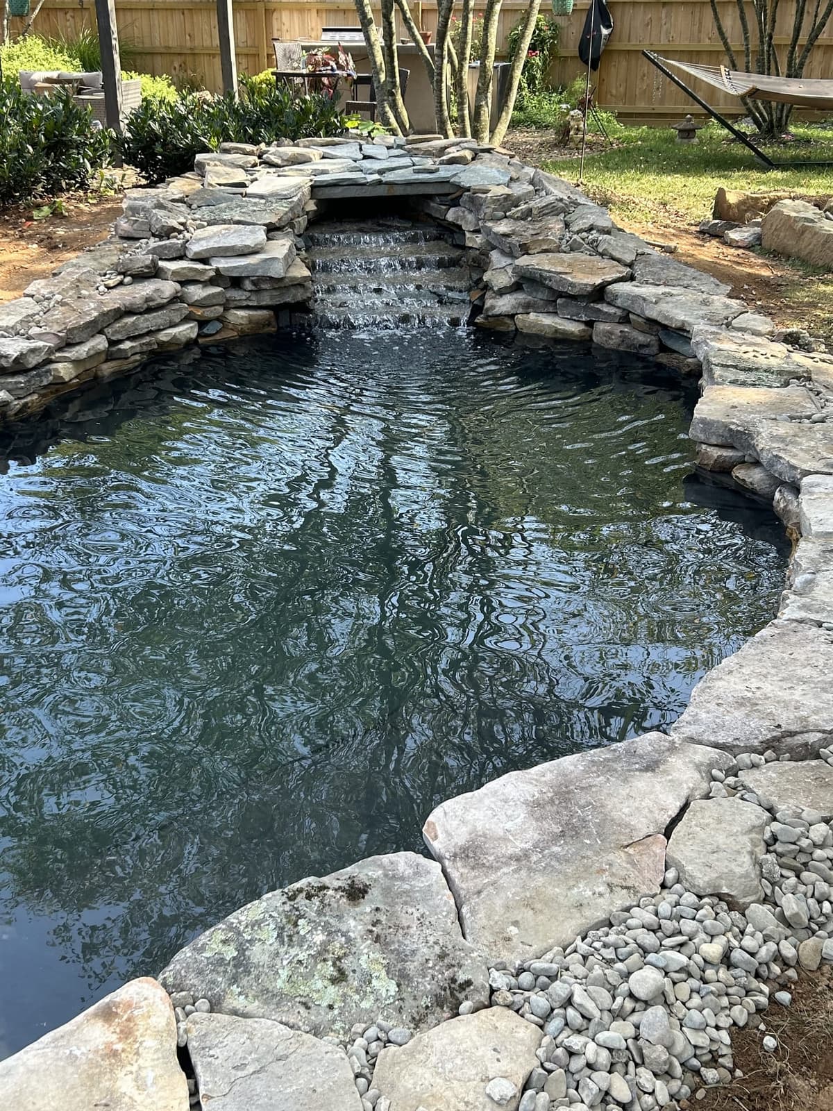 Backyard koi pond with stacked-stone waterfall by Diamond Pond